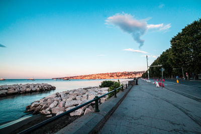 People on footpath by sea against blue sky