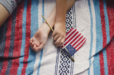 High angle view of hand holding american flag while lying on bed