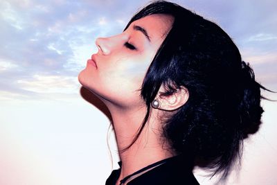 Side view close-up of young woman with closed eyes against sky