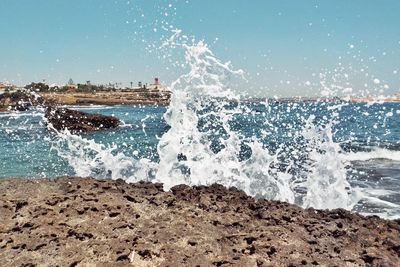 Waves splashing on rocks at beach against sky