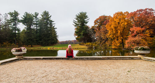 Man sitting by lake against sky during autumn