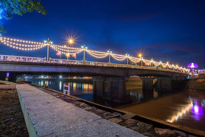 Illuminated bridge over river against sky at night