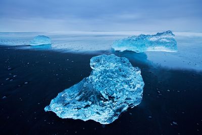 Close-up of ice crystals on sea shore against sky