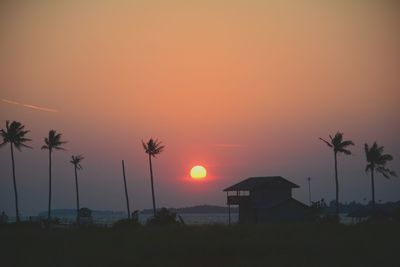 Silhouette palm trees on field against romantic sky at sunset