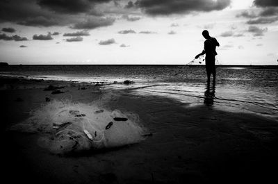 Silhouette fisherman with net at beach against sky