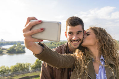 Girlfriend taking selfie with boyfriend against sky