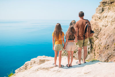 Rear view of people standing on rock by sea