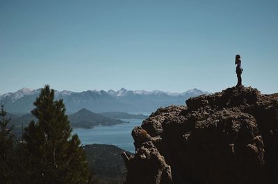 Side view of man standing on rock against sky