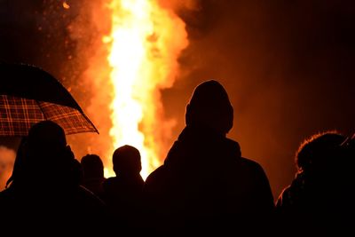 Silhouette people looking at fire against sky during night