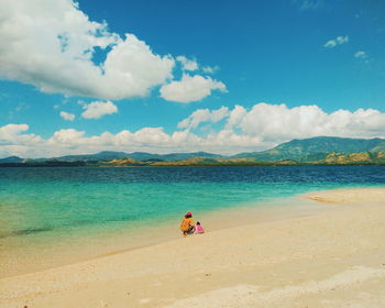 Mother and child crouching on shore at beach against sky