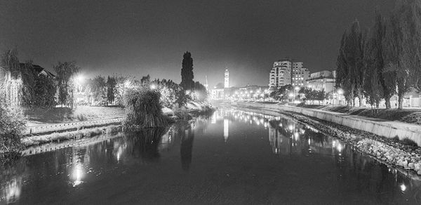 Panoramic view of river by illuminated buildings against sky at night