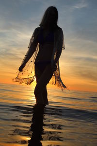 Woman standing on beach against sky during sunset