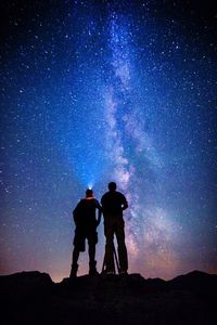 Low angle view of silhouette men standing against star field at night