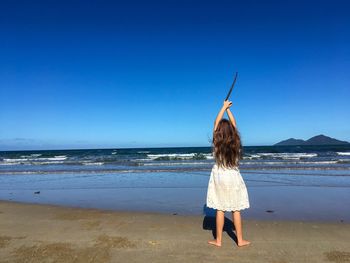 Rear view of woman standing on beach against clear blue sky