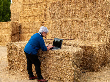 Woman using laptop on hay bales at field