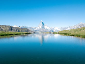 Scenic view of lake and mountains against clear blue sky