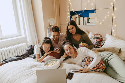 Cheerful multiracial friends watching movie together on laptop at home