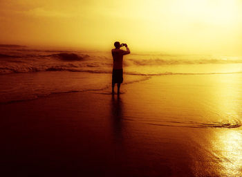 Man standing on wet beach against sky during sunset