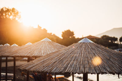 Thatched roof at beach against sky during sunset