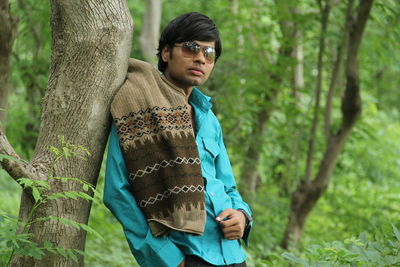 Young man standing by tree trunk in forest