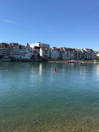 Buildings by sea against clear blue sky