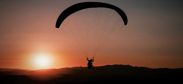 Silhouette person paragliding against sky during sunset