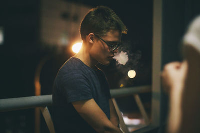 Side view of man smoking in balcony at night