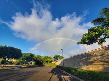 Rainbow over road by trees against sky