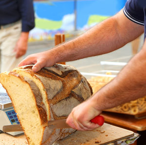 Young baker cuts a loaf of freshly baked bread at the bakery