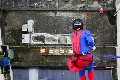 Man dressed as a superhero rappelling down from a tall building. 