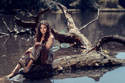 Portrait of young woman sitting on tree trunk in water