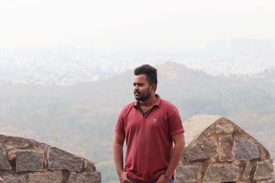 Young man standing on wall against mountain