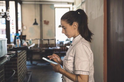 Side view of female chef using smart phone in restaurant