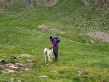 Hiker standing by dog on grassy field