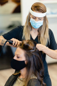 Hairdresser wearing mask styling woman hair in salon