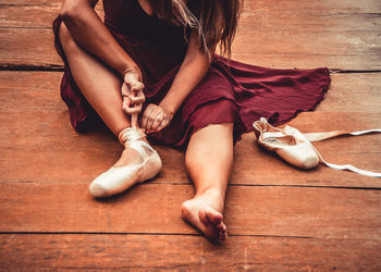 Low section of woman fastening ballet shoe on hardwood floor