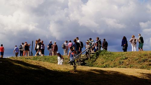 Low angle view of people standing on hill against cloudy sky