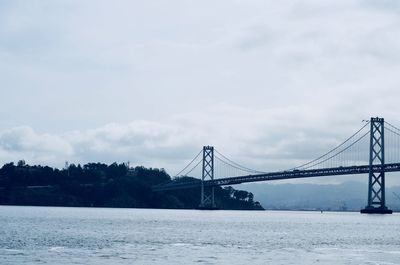 Suspension bridge over river against cloudy sky