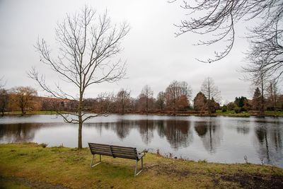 Park bench by lake against sky