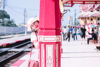 Portrait of smiling woman standing behind pillar on railroad station platform