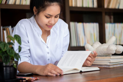 Young woman reading book at table in library