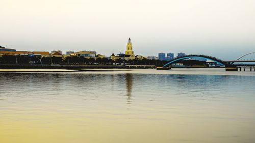 Bridge over river by buildings against sky during sunset