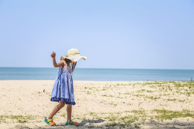 Full length of girl walking on sand at beach against clear sky