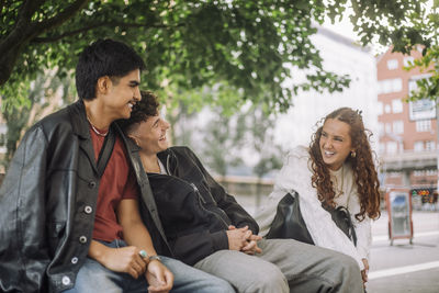 Teenage male and female friends laughing together while sitting on bench
