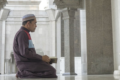 Side view of mature man reading koran while kneeling at mosque