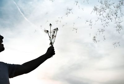 Man holding dandelions against sky