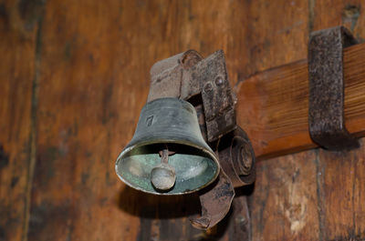 Close-up of rusty metallic bell hanging on wooden wall