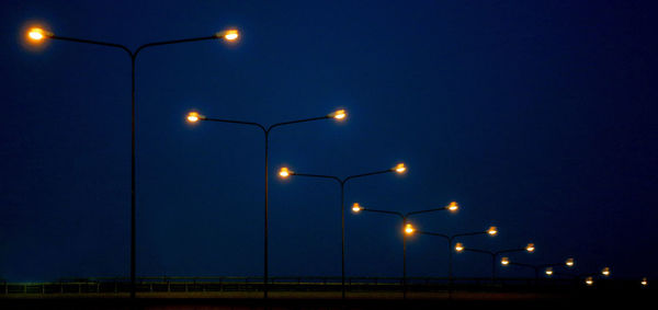 Low angle view of illuminated street lights against blue sky