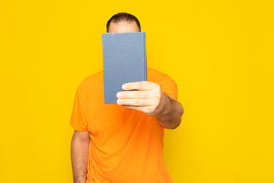 Midsection of woman holding book against yellow background