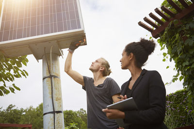 Low angle view of garden architect adjusting solar panel by colleague holding tablet computer